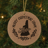 Brown leatherette round Christmas ornament engraved Merry Christmas From New Hampshire, with the state shape in a laurel wreath, hanging on a tree