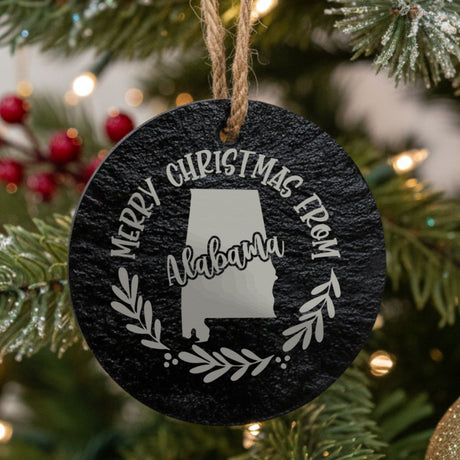 Round slate Christmas ornament engraved Merry Christmas From Alabama, with the state shape in a laurel wreath