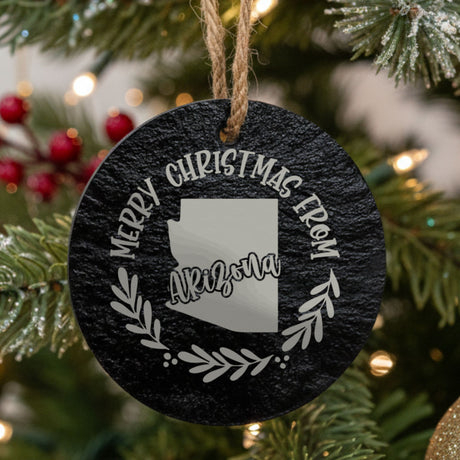 Round slate Christmas ornament engraved Merry Christmas From Arizona, with the state shape in a laurel wreath