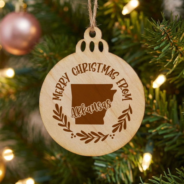 Round wood Christmas ornament engraved Merry Christmas From Arkansas, with the state shape in a laurel wreath