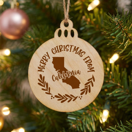 Round wood Christmas ornament engraved Merry Christmas From California, with the state shape in a laurel wreath
