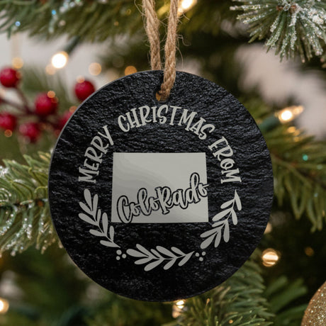 Round slate Christmas ornament engraved Merry Christmas From Colorado, with the state shape in a laurel wreath