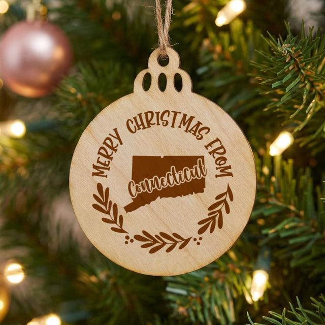 Round wood Christmas ornament engraved Merry Christmas From Connecticut, with the state shape in a laurel wreath