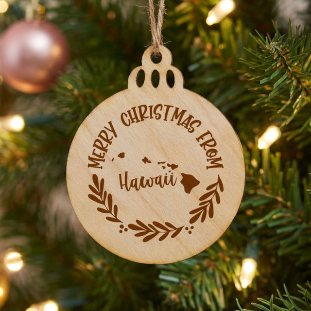 Round wood Christmas ornament engraved Merry Christmas From Hawaii, with the state shape in a laurel wreath