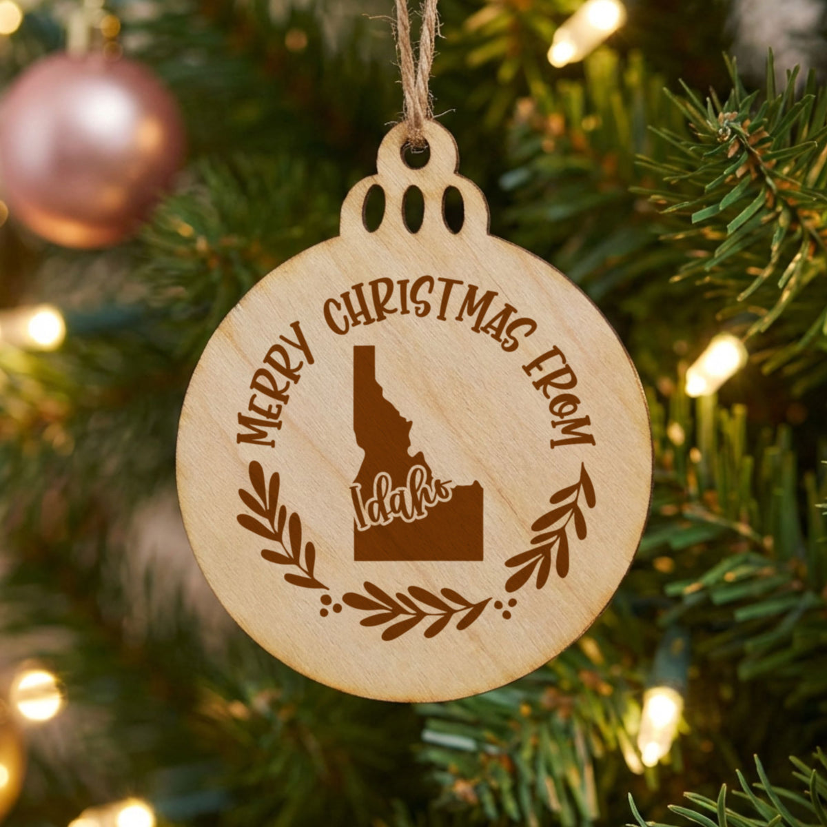 Round wood Christmas ornament engraved Merry Christmas From Idaho, with the state shape in a laurel wreath