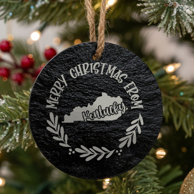 Round slate Christmas ornament engraved Merry Christmas From Kentucky, with the state shape in a laurel wreath