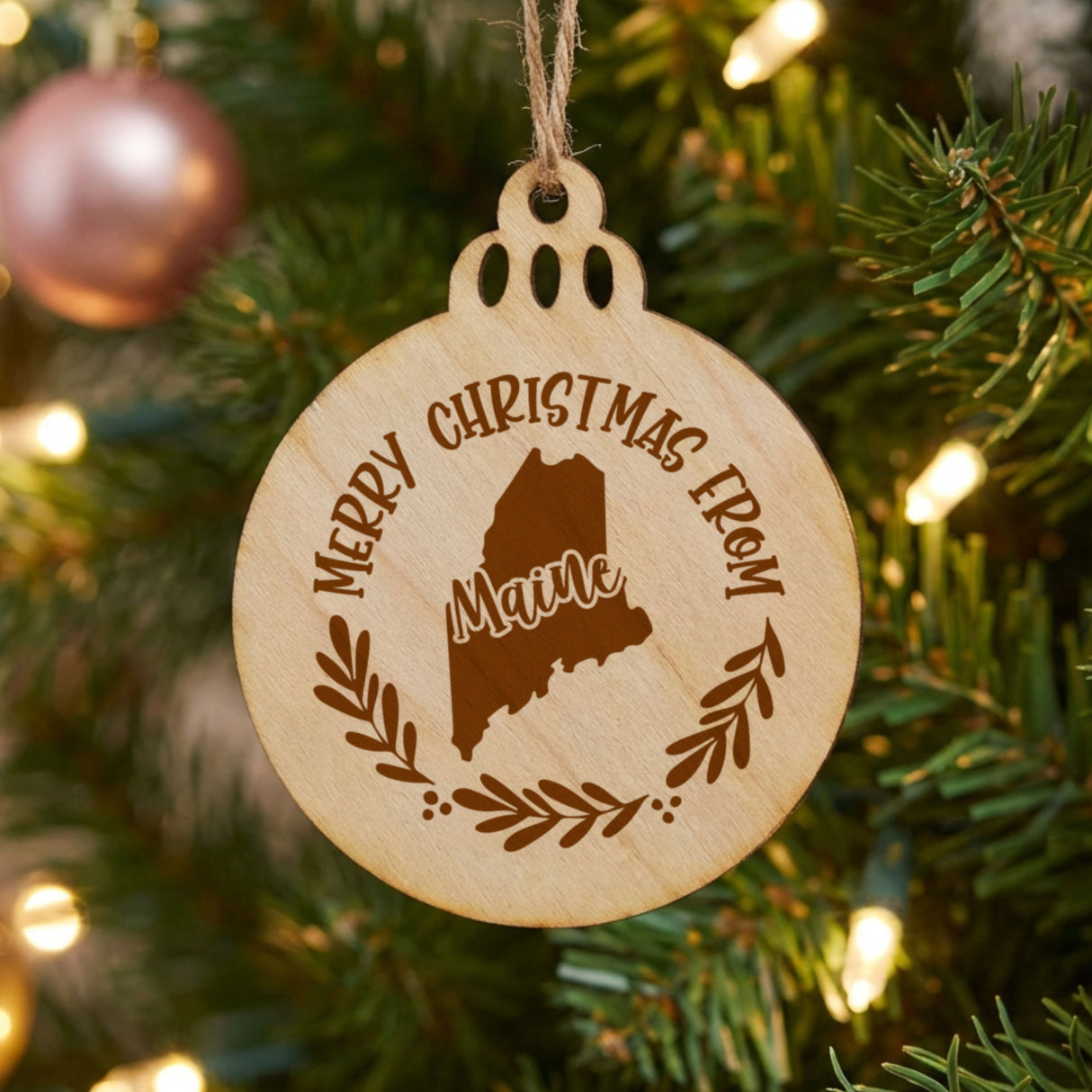 Round wood Christmas ornament engraved Merry Christmas From Maine, with the state shape in a laurel wreath