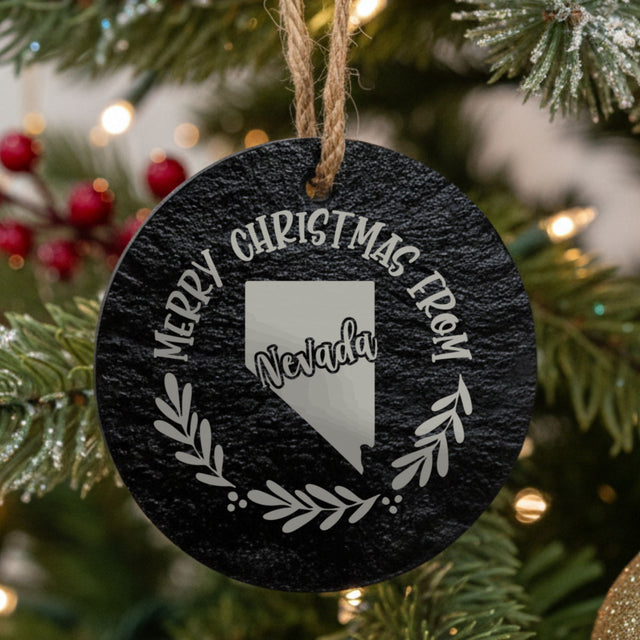 Round slate Christmas ornament engraved Merry Christmas From Nevada, with the state shape in a laurel wreath