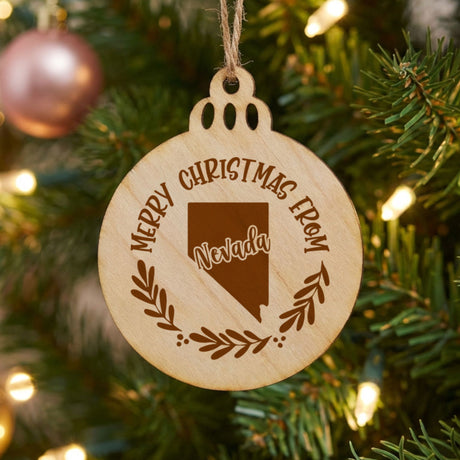 Round wood Christmas ornament engraved Merry Christmas From Nevada, with the state shape in a laurel wreath