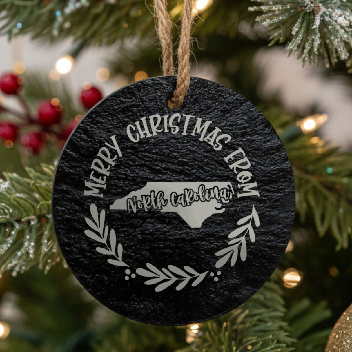 Round slate Christmas ornament engraved Merry Christmas From North Carolina, with the state shape in a laurel wreath