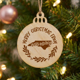 Round wood Christmas ornament engraved Merry Christmas From North Carolina, with the state shape in a laurel wreath
