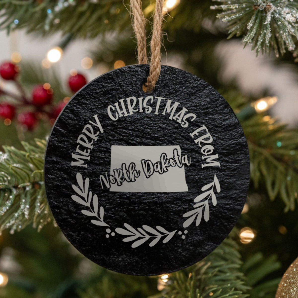 Round slate Christmas ornament engraved Merry Christmas From North Dakota, with the state shape in a laurel wreath