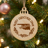 Round wood Christmas ornament engraved Merry Christmas From Oklahoma, with the state shape in a laurel wreath