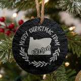 Round slate Christmas ornament engraved Merry Christmas From Oregon, with the state shape in a laurel wreath