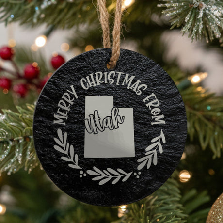 Round slate Christmas ornament engraved Merry Christmas From Utah, with the state shape in a laurel wreath