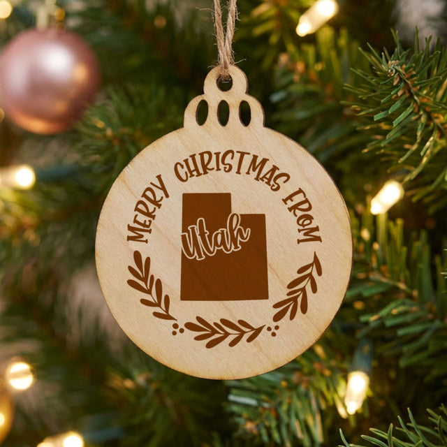 Round wood Christmas ornament engraved Merry Christmas From Utah, with the state shape in a laurel wreath