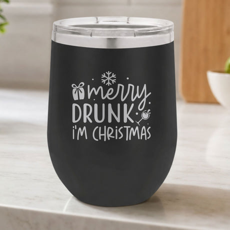 Black 12 oz stemless wine tumbler laser engraved with "Merry Drunk, I'm Christmas", on a kitchen counter