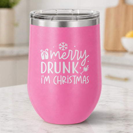 Pink 12 oz stemless wine tumbler laser engraved with "Merry Drunk, I'm Christmas", on a kitchen counter