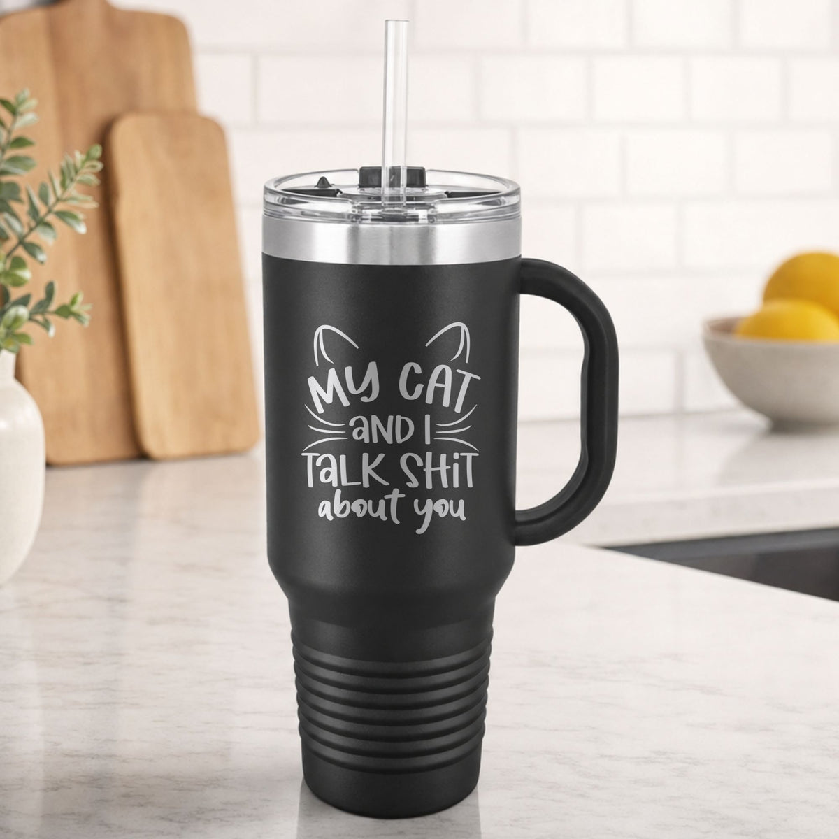 Black 40 oz tumbler with handle and straw laser engraved with "My Cat and I Talk Sh*t About You", plus cat ears and whiskers, on a kitchen counter
