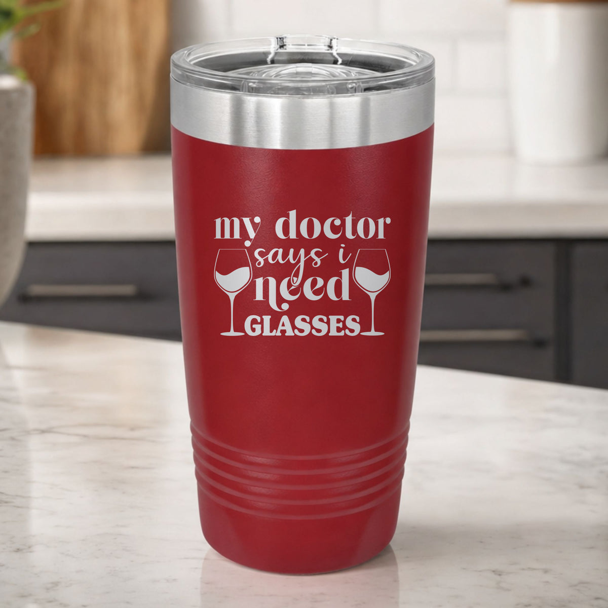 Maroon 20 oz tumbler laser engraved with "My Doctor Says I Need Glasses", on a kitchen counter