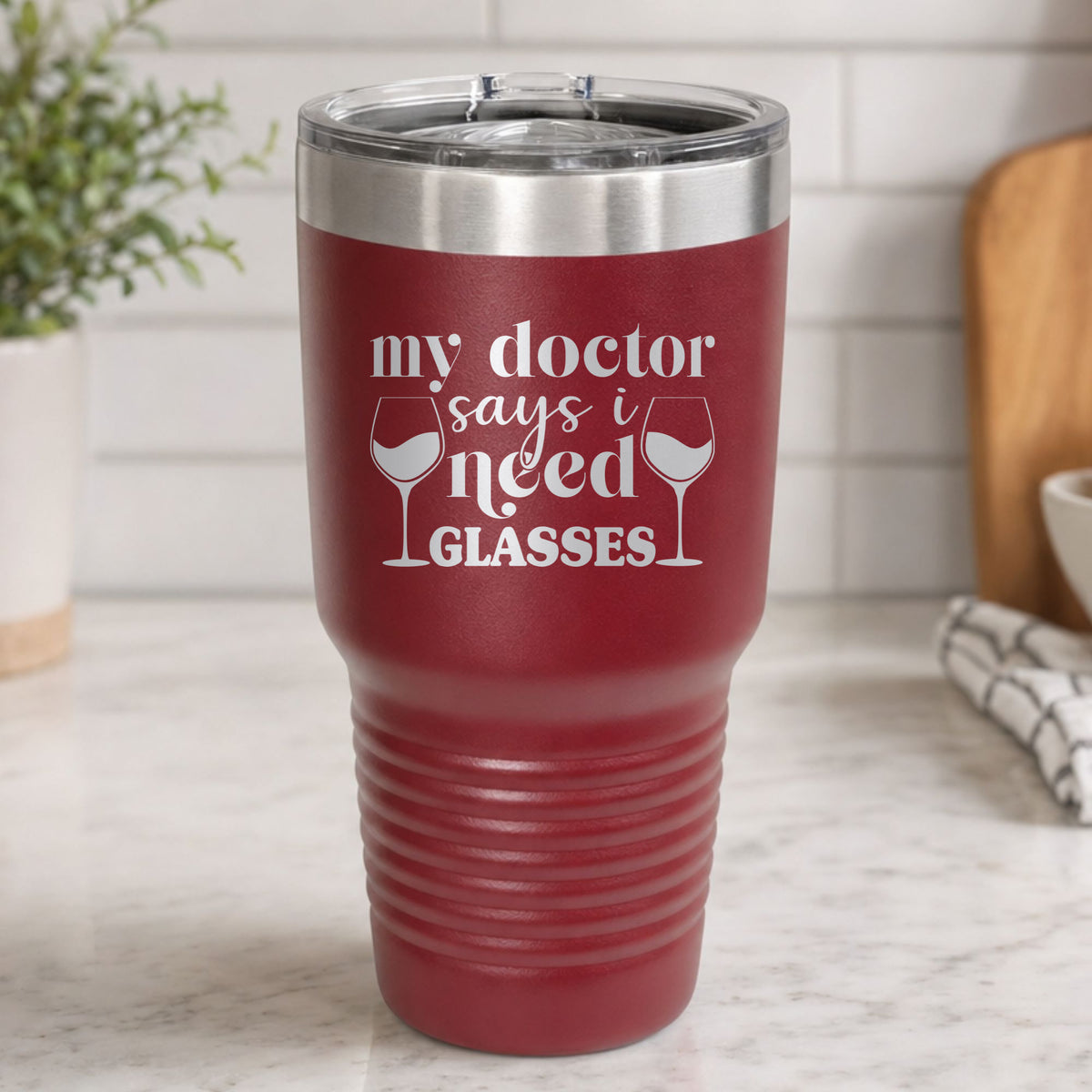 Maroon 30 oz tumbler laser engraved with "My Doctor Says I Need Glasses", on a kitchen counter