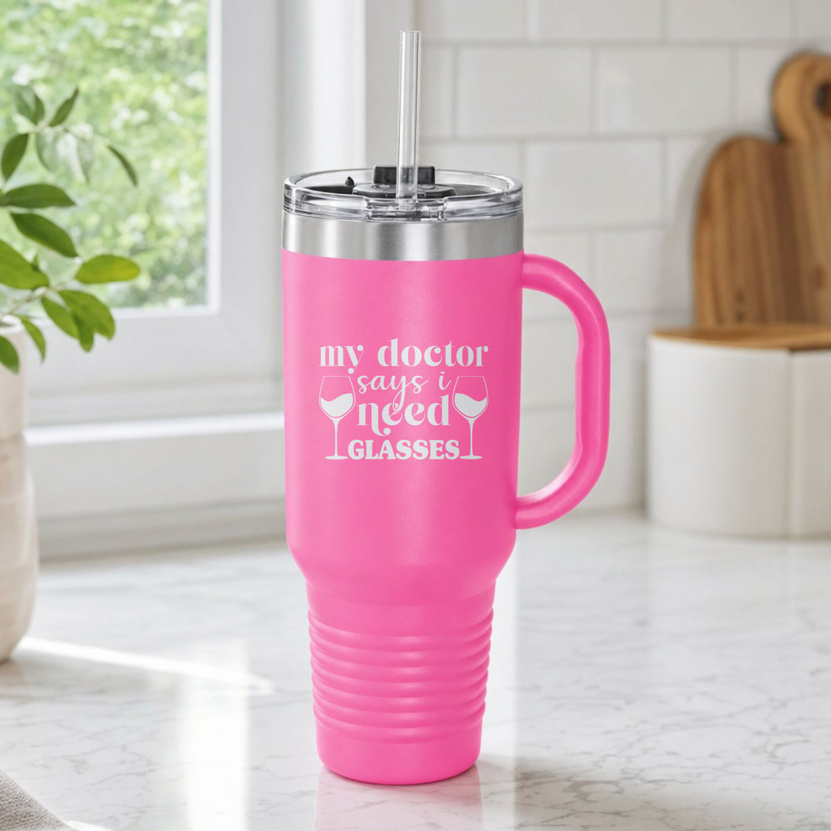 Pink 40 oz tumbler with handle and straw laser engraved with "My Doctor Says I Need Glasses", on a kitchen counter