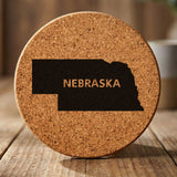 Nebraska round cork coaster engraved with the state shape and NEBRASKA in bold lettering