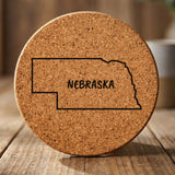 Nebraska round cork coaster engraved with the state outline and NEBRASKA in hand-drawn brush lettering