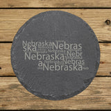 Nebraska round slate coaster engraved with a word cloud of repeating Nebraska text