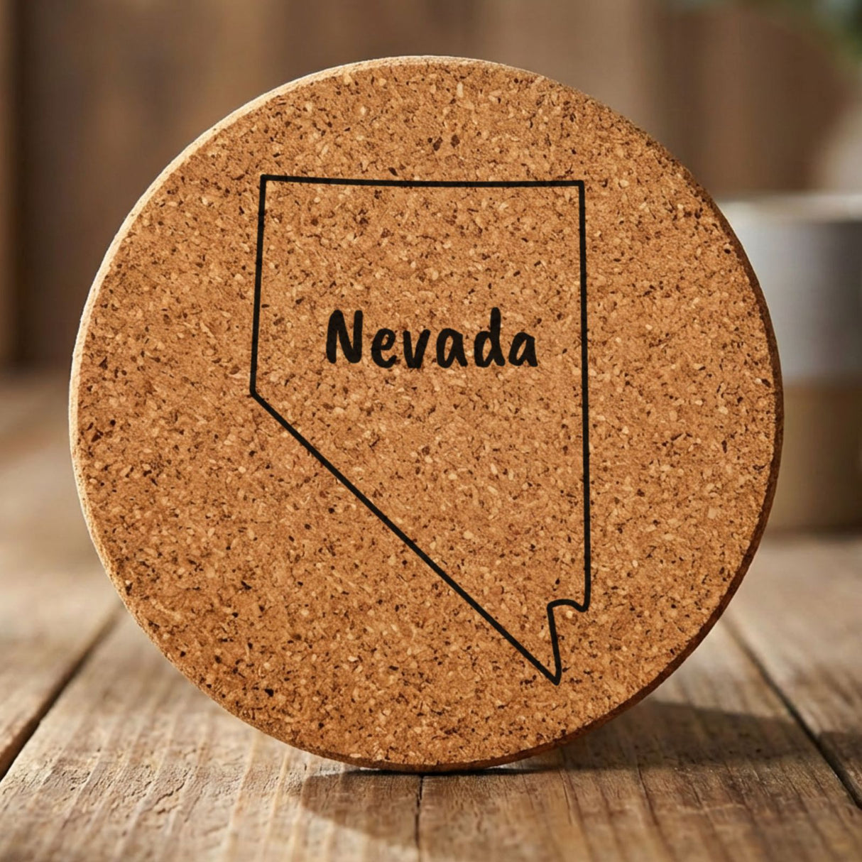 Nevada round cork coaster engraved with the state outline and NEVADA in hand-drawn brush lettering