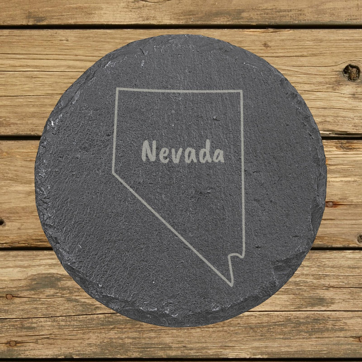 Nevada round slate coaster engraved with the state outline and NEVADA in hand-drawn brush lettering