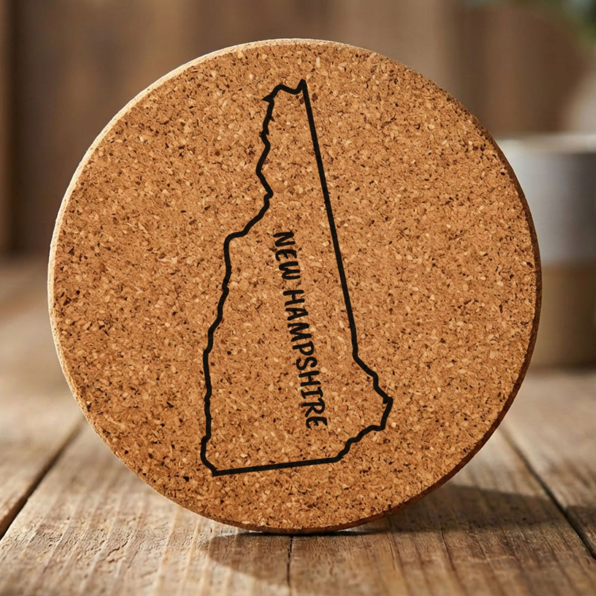 New Hampshire round cork coaster engraved with the state outline and NEW HAMPSHIRE running vertically