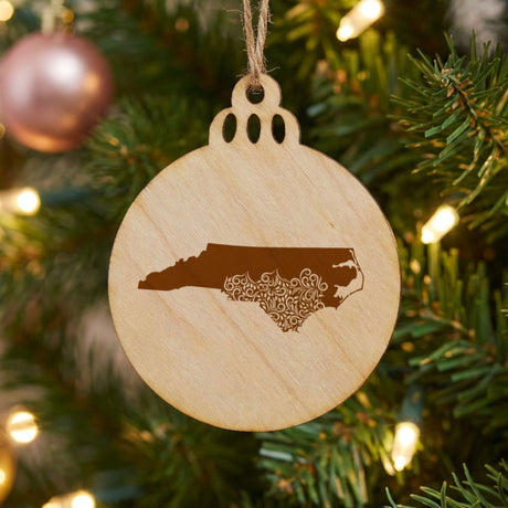 North Carolina round wood Christmas ornament engraved with the state shape in ornate floral scrollwork