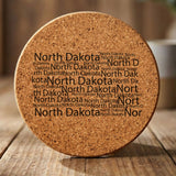 North Dakota round cork coaster engraved with a word cloud of repeating North Dakota text