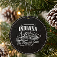 Black leatherette round Christmas ornament laser engraved with an Indiana design of a red barn, a race car and a torch, hanging on a tree
