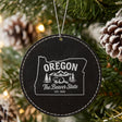 Black leatherette round Christmas ornament laser engraved with an Oregon design of a beaver, mountains and pines, hanging on a tree