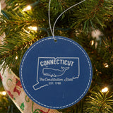Blue leatherette round Christmas ornament laser engraved with a Connecticut design of a sperm whale, hanging on a tree