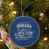 Blue leatherette round Christmas ornament laser engraved with an Indiana design of a red barn, a race car and a torch, hanging on a tree