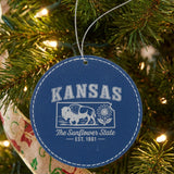 Blue leatherette round Christmas ornament laser engraved with a Kansas design of a bison and a sunflower, hanging on a tree