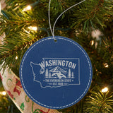 Blue leatherette round Christmas ornament laser engraved with a Washington design of an orca, Mount Rainier and evergreens, hanging on a tree