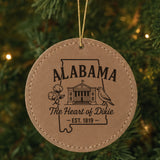 Brown leatherette round Christmas ornament laser engraved with an Alabama design of the capitol building, a cotton boll and a yellowhammer, hanging on a tree