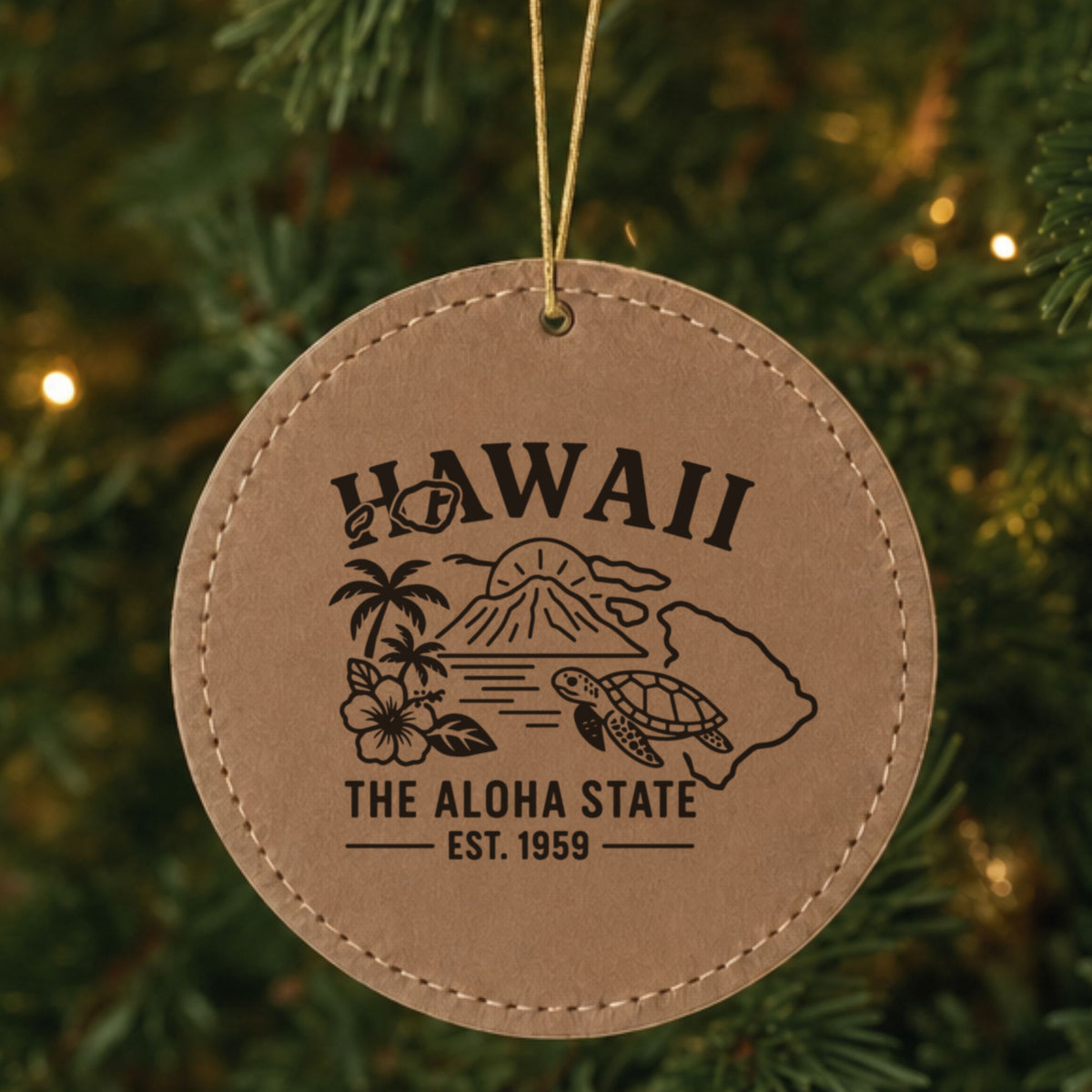 Brown leatherette round Christmas ornament laser engraved with a Hawaii design of a volcano, palm trees, a hibiscus and a sea turtle, hanging on a tree