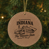 Brown leatherette round Christmas ornament laser engraved with an Indiana design of a red barn, a race car and a torch, hanging on a tree
