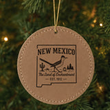 Brown leatherette round Christmas ornament laser engraved with a New Mexico design of a roadrunner, cactus and pines, hanging on a tree