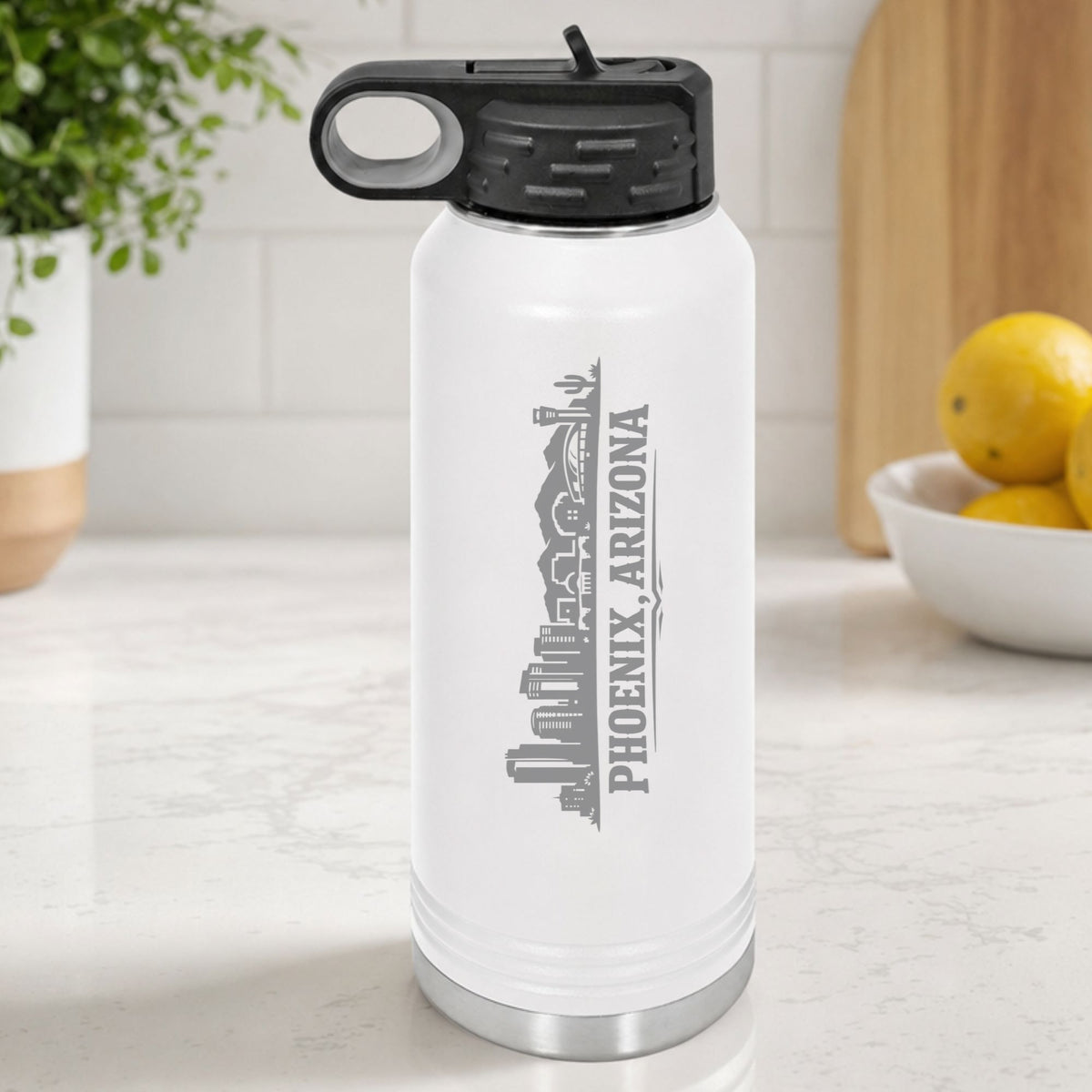 White 32 oz insulated water bottle laser engraved with the Phoenix, Arizona skyline running up the side, standing on a kitchen counter