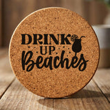 Round cork coaster laser engraved with "Drink Up Beaches"