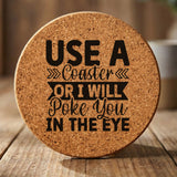 Round cork coaster laser engraved with "Use a Coaster or I Will Poke You in the Eye", hand lettered design