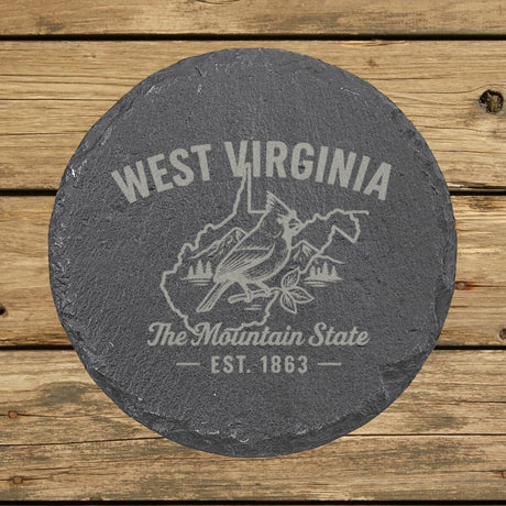 West Virginia round slate coaster engraved with the state outline, a cardinal, mountains and pines, "The Mountain State"