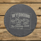 Wyoming round slate coaster engraved with the state outline, a cowboy on horseback, a bighorn sheep and mountains, "The Cowboy State"