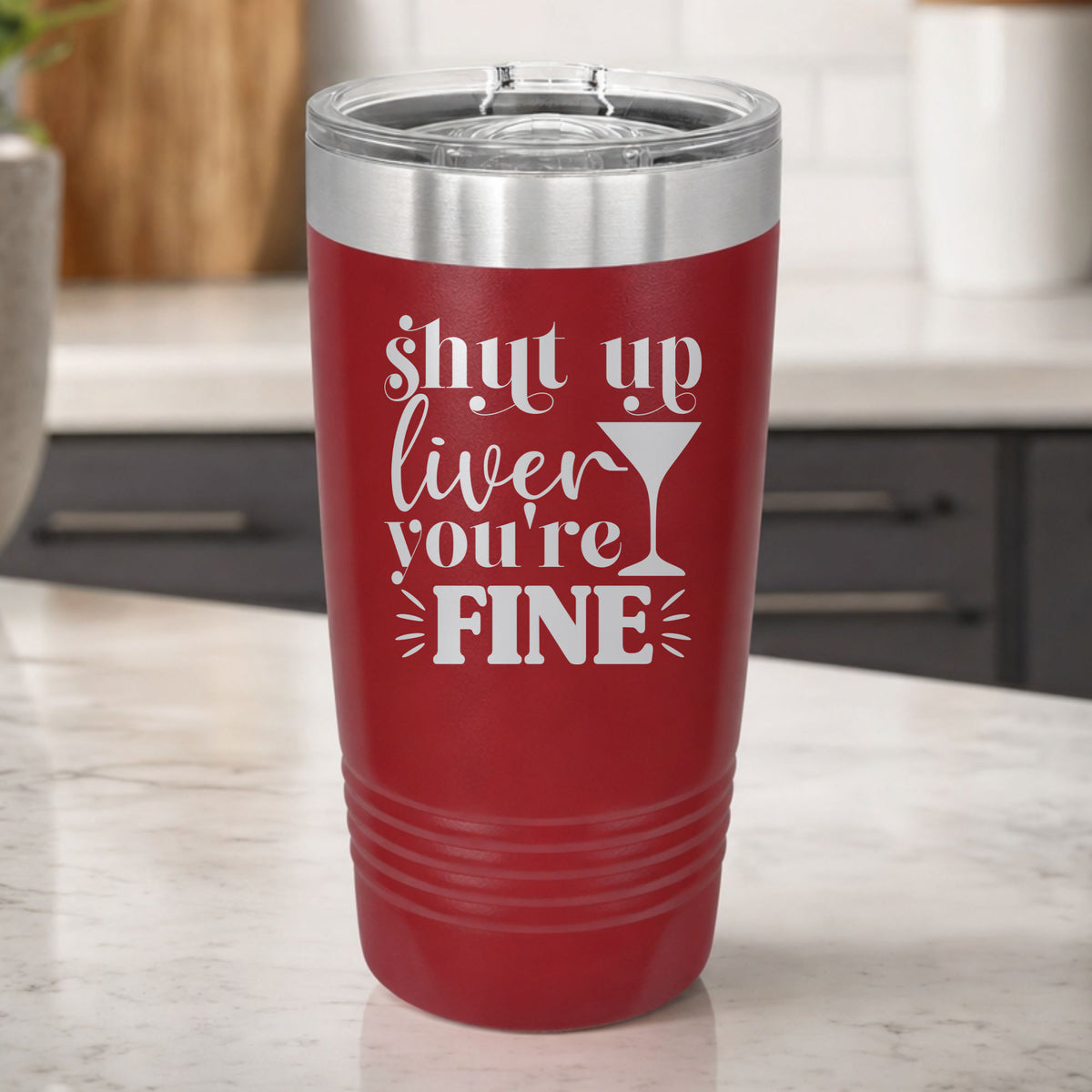 Maroon 20 oz tumbler laser engraved with "Shut Up Liver, You're Fine", on a kitchen counter